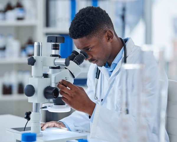A professional black scientist examines samples using a microscope in a modern laboratory setting.